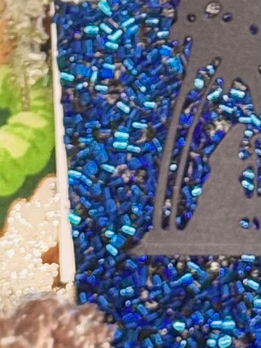 Close-up of a textured surface with blue tightly rolled ribbon to look like beadsand black silhouette of Nativity die-cut showing the palm tree and shepherd with staff.