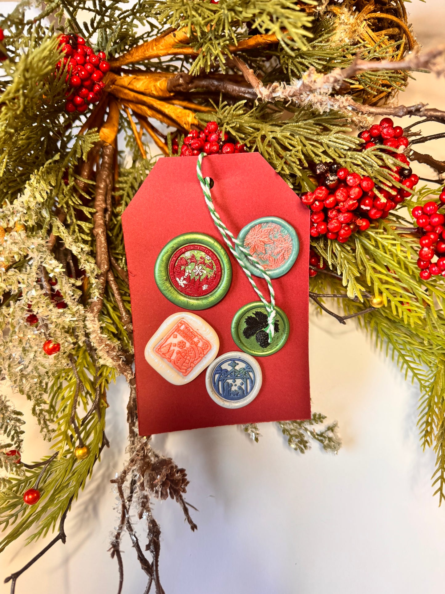 Decorative Red gift tag with red and white twine, with five decorative wax seals. eindeer and evergreen trees and greeting: "Christmas is a letter in winter and the end of the year is a signal to return home" pink snowflakes (3D) and teal background, the bottom left is a white, pink snowman and snowflakes with the greeting Merry Christmas, gray and navy blue with a scene of palm trees, Nativity Scene and star, and the bottom right is green background with a black leafy pine cone.