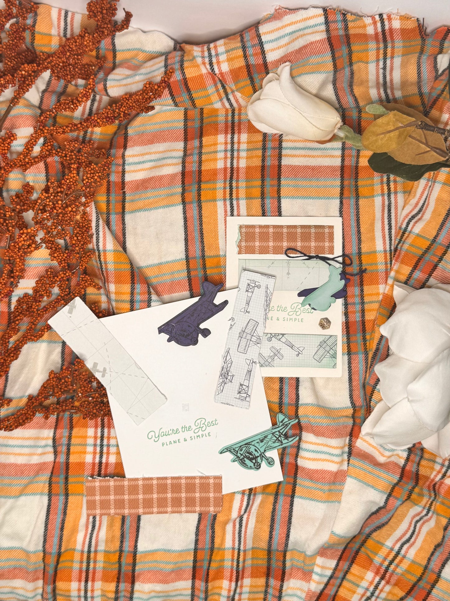 This card nods to aviation history, with layered textures and flight-inspired imagery. But it’s more than a clever pun. It’s a way to honor those who served with simplicity and respect. Whether you're sending it to a veteran or someone who simply shows up for others in quiet ways, this card is a steady expression of gratitude. including aviation paper to attach and two planes. Autumn-themed items including a plaid blanket, decorative branches, and stationery on a matching fabric background.