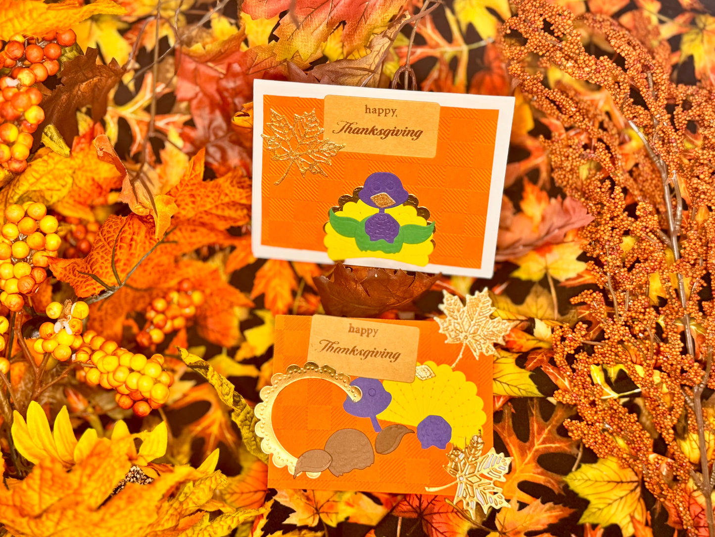 Two A Thanksgiving classic with embossed checkered paper, two maple leaves, and a detailed-layered turkey with four layers of feathers. with pumpkins and berries on a bed of autumn leaves and berries.
