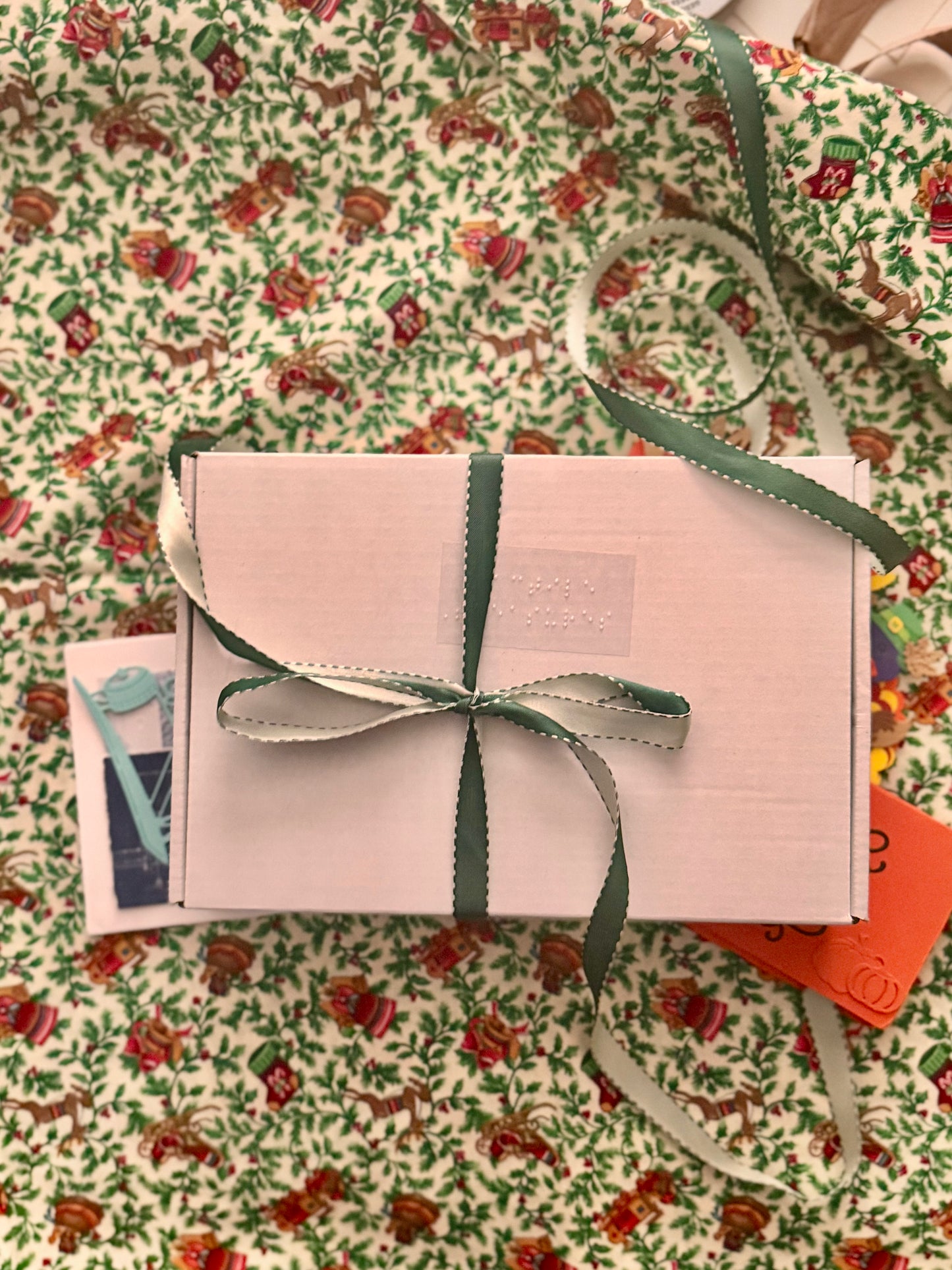 Give the Gift of our October Subscription box with green ribbon on a Christmas holly floral-patterned surface