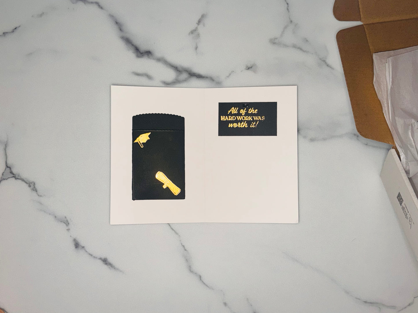 Gift card holder/money holder in black with a gold foil diploma attached, and small black and gold graduation cap, on the inside right panel is a small black rectangle with gold embossed greeting: All the hard work paid off!