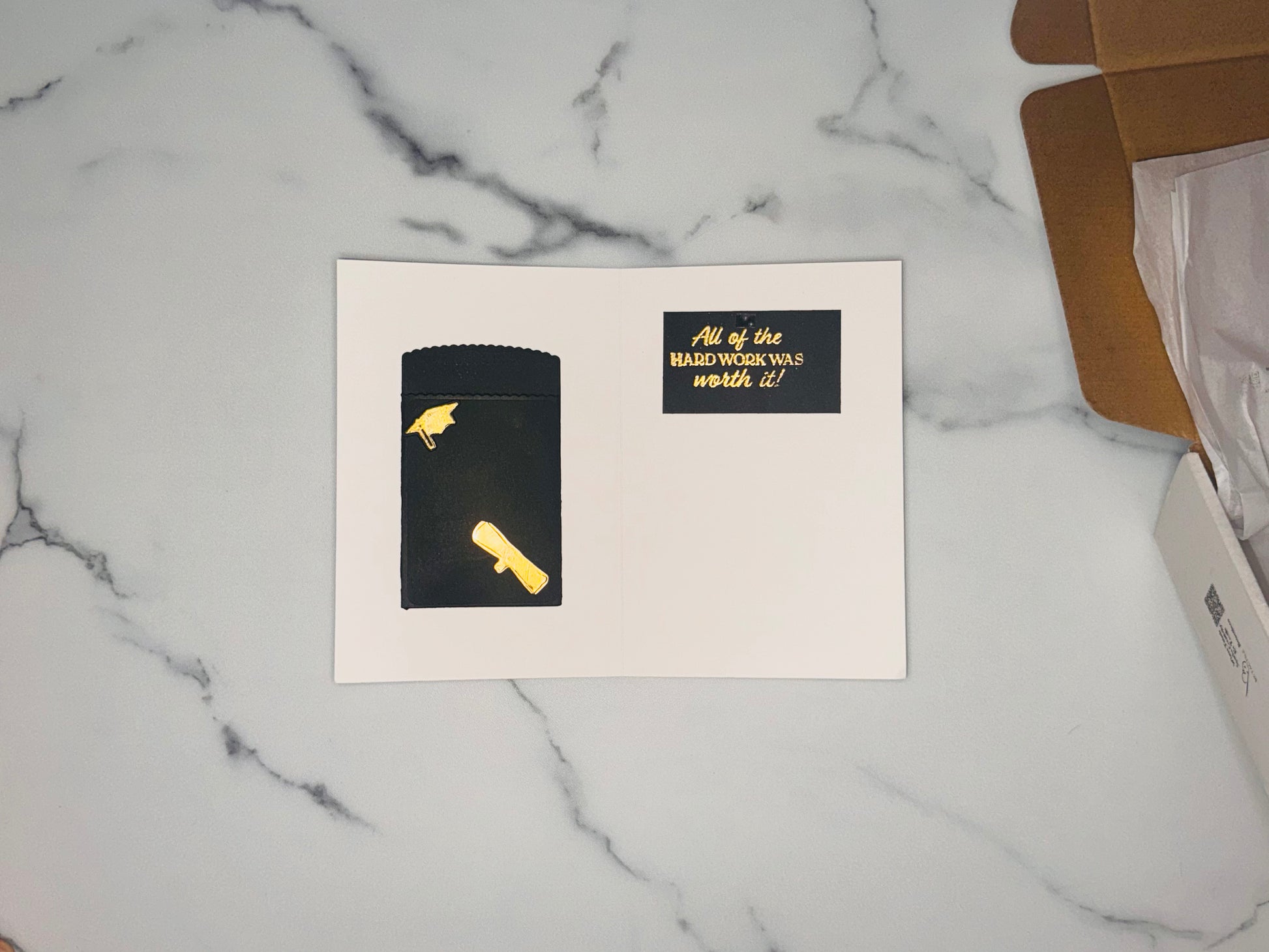 Gift card holder/money holder in black with a gold foil diploma attached, and small black and gold graduation cap, on the inside right panel is a small black rectangle with gold embossed greeting: All the hard work paid off!