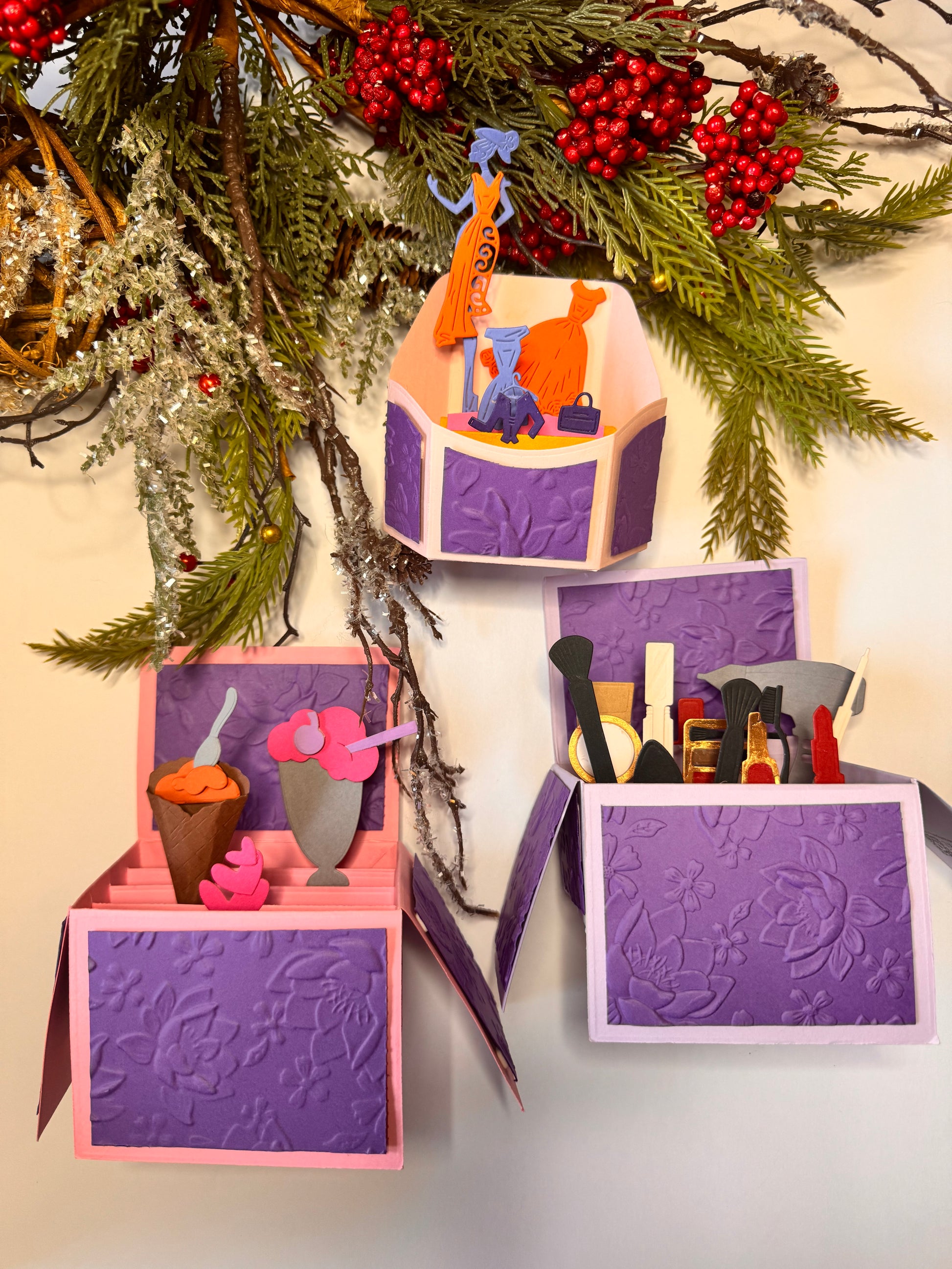 Three pre-made popup cards with embossed purple flowers paper with pink background and popup box. Each box’s front panel is open, revealing its contents. an ice cream cone, pink hearts,  milkshake glass with pink ice cream, a purple cherry and straw.