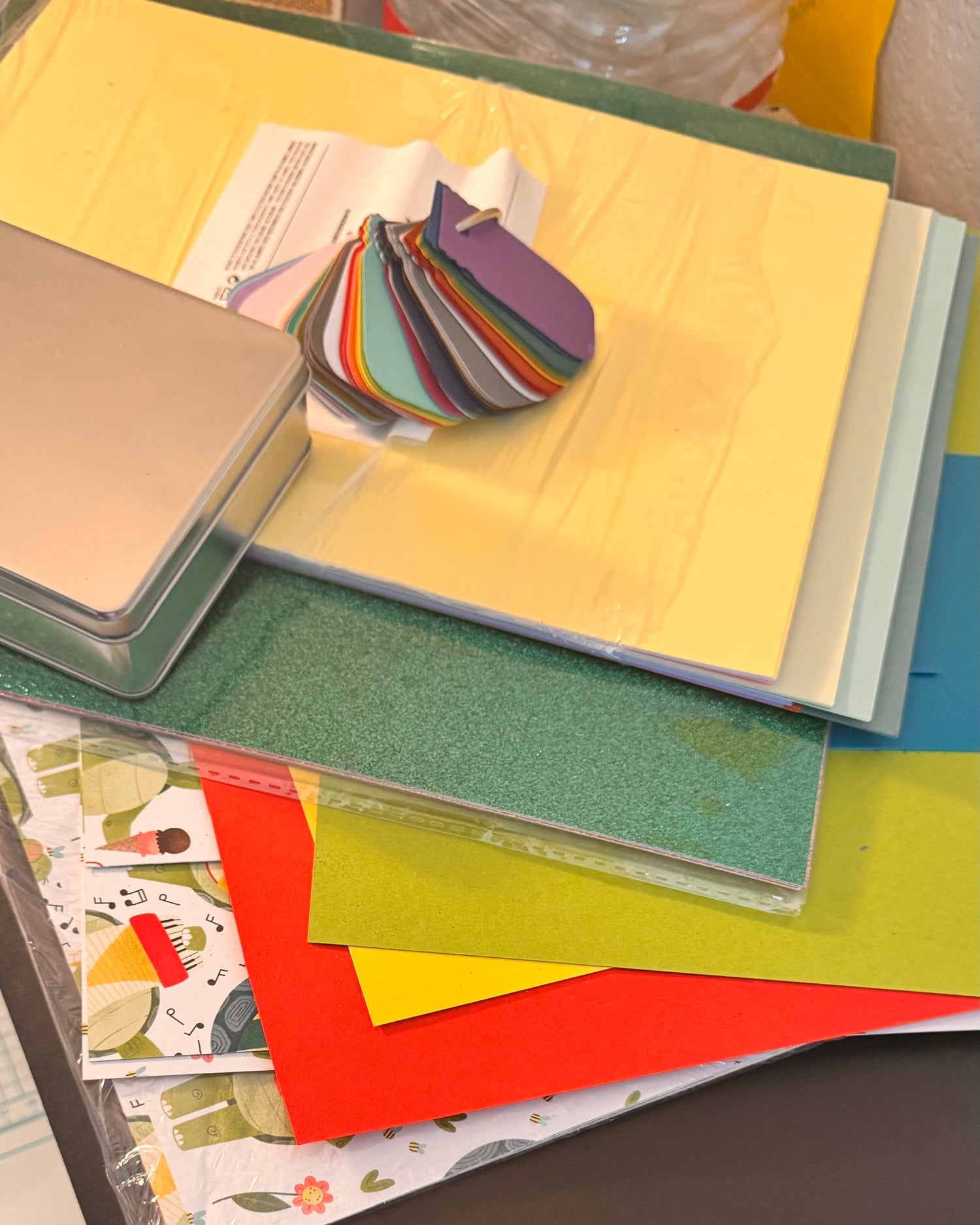 some supplies shows, multiple shades of green paper stack, glitter cardstock, red and yellow yardsticks, turtle designer paper, not shown is metal dies, ribbon and embellishments to add texture to piece of art.