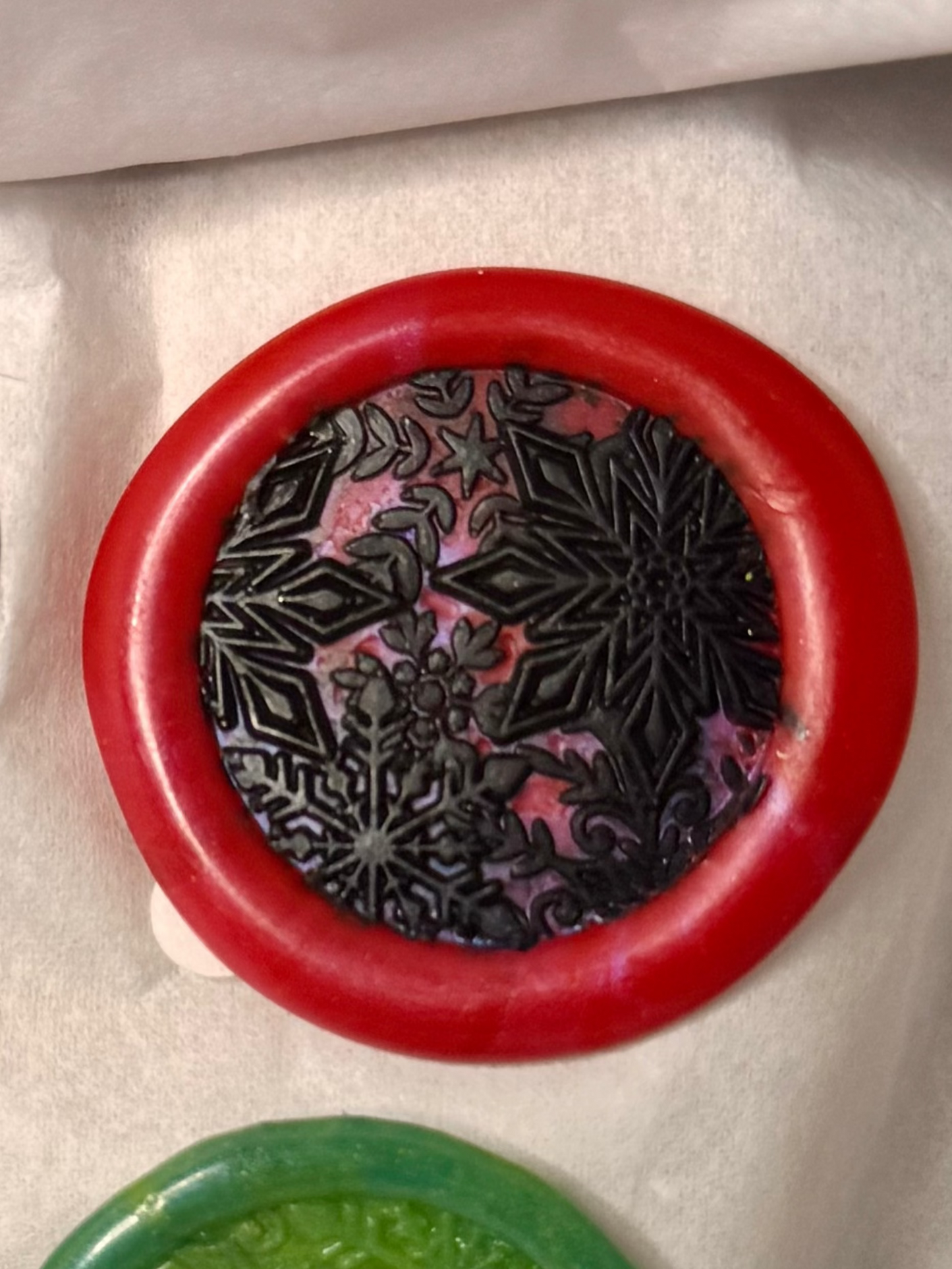 round wax seal with an outer edge. The center of the seal has an intricate design, featuring snowflake-like dimensional  star-shaped patterns. 