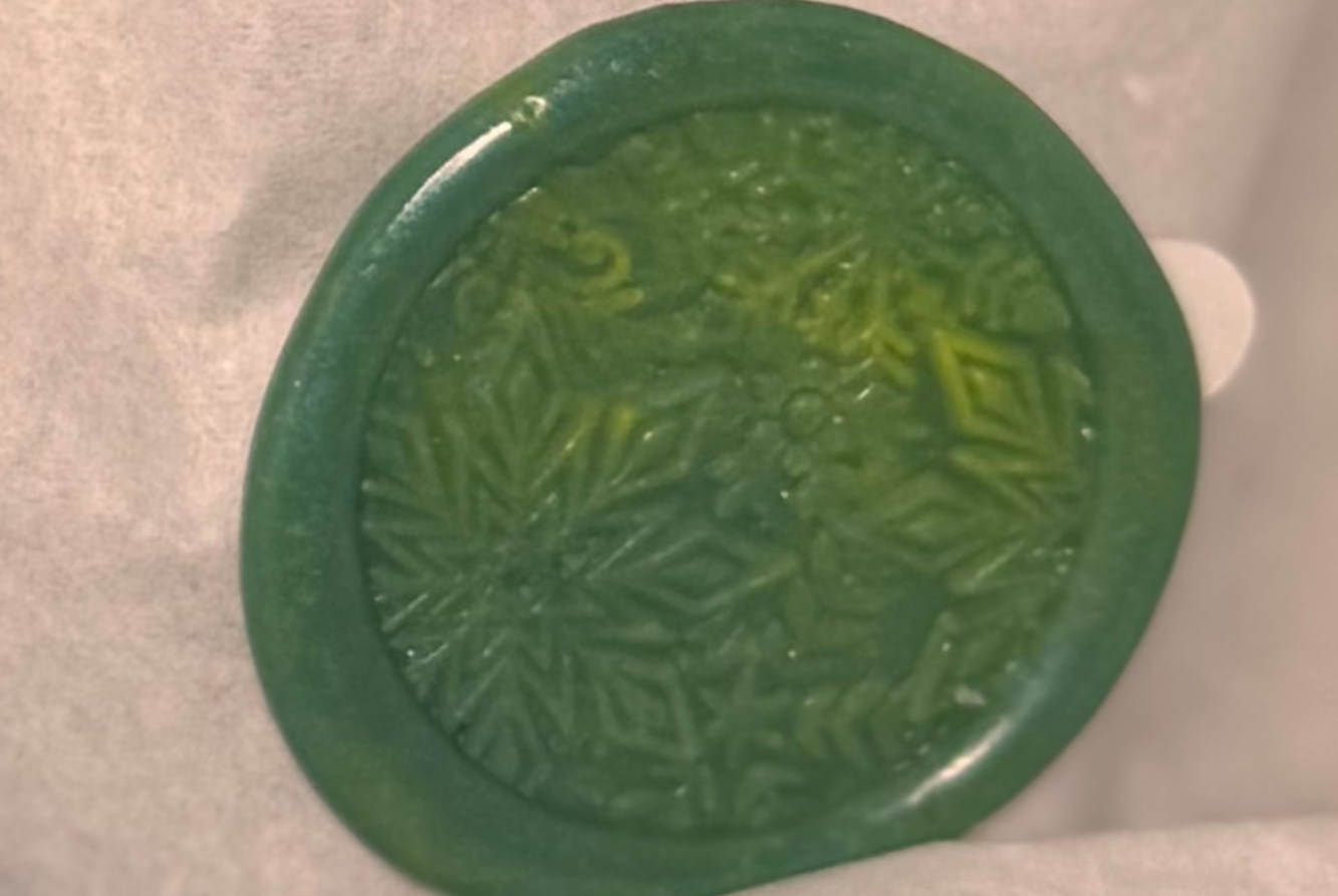 round wax seal with an outer edge. The center of the seal has an intricate design, featuring snowflake-like dimensional  star-shaped patterns. 