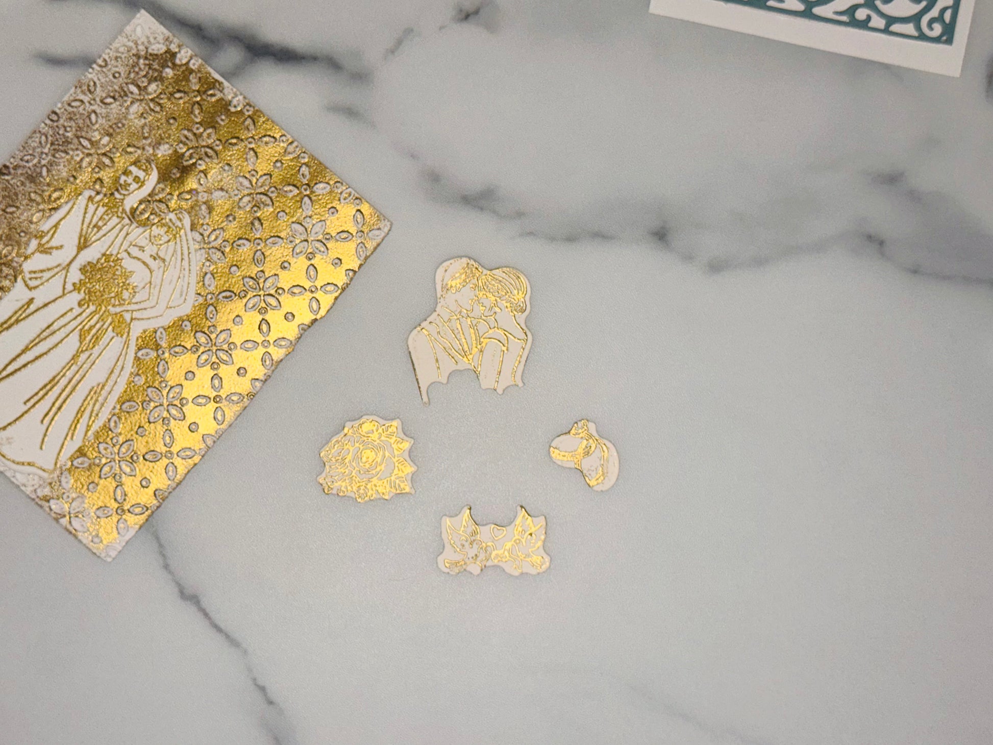 Accent pieces to add to wedding card: a small white cutout with gold line art of two interlocking wedding rings a small white cutout with gold line art of two dove birds, a piece of ribbon held between there beaks a small white cutout with gold line art of a rose (flower head with layered petals) a medium white cutout with gold line art of a couple in an embrace (upper bodies close together)